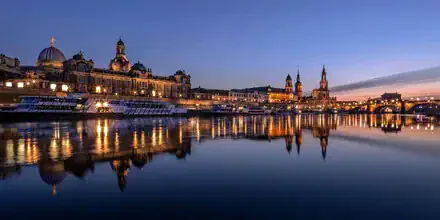 Dresden bei Nacht: beleuchtete Silhouette von Semperoper und Frauenkirche am Elbufer.