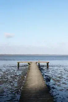 Wadden Sea at low tide with a calm wooden pier near the beach.