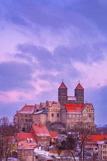 A winter view of Quedlinburg with snow-covered rooftops and the castle.