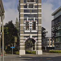 The striking striped architecture of the historic New Plymouth Clock Tower in the city center. The historic New Plymouth Clock Tower, featuring a tall grey and white striped stone design with a white dome on top, standing at a street corner under a blue sky with soft clouds.