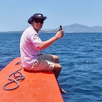 A traveler relaxing on a boat in the Philippines, showcasing the beauty of island hopping and tropical adventures. Enjoying a relaxing moment on a boat with a drink, surrounded by clear blue waters and scenic island.