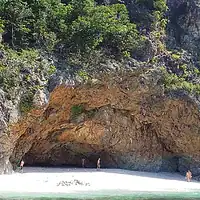 Beautiful beach with a prominent cave entrance, surrounded by lush vegetation, perfect for island hopping adventures in the Philippines. Scenic beach with a large cave entrance and lush greenery in the Philippines.