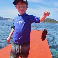 Happy child with a fish on a boat dock during a family fishing trip in the Philippines. Child holding a fish on a boat dock with scenic ocean view.