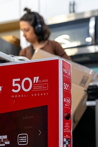 High-quality 50-inch TCL smart TV box with HDMI and Dolby audio, being unpacked in a tech store or home setup.