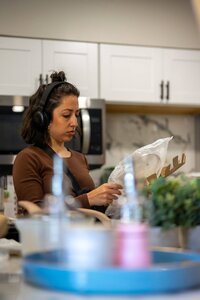 A woman in a kitchen wearing headphones examines a floral centerpiece, showcasing a cozy, stylish culinary space.
