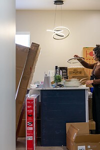 Photo of a woman packing or unpacking kitchen items during a move, surrounded by boxes and packing materials indoors.