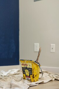 Paint bucket with brush on a cloth covering the floor during room painting.