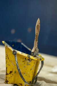An image of a yellow paint bucket with a paintbrush inside, used for construction and painting projects.