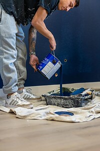 Young man pouring blue paint into a tray during a home renovation.