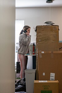 Woman on phone amid moving boxes in a new home, preparing for a move or unpacking.