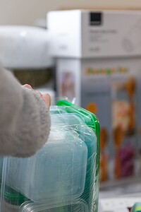 Close-up of hands organizing clear plastic containers with green lids for children's toys and art supplies.