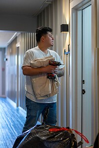 Image of a young male technician fixing an elevator door with tools in hand.
