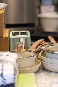 Versatile pots, pans, and kitchen utensils arranged on marble countertop in chef's studio.