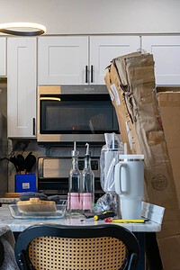 A messy kitchen with moving boxes, appliances, and essentials, indicating a recent or ongoing move or renovation project.