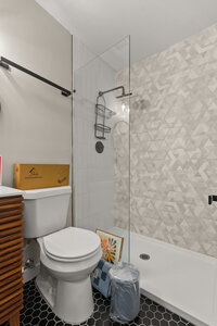Bathroom with walk-in shower, white toilet, and decorative tiled wall.
