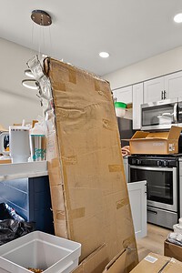 Alt text: Cardboard moving boxes in a sleek, modern kitchen with white cabinets and stainless steel appliances.