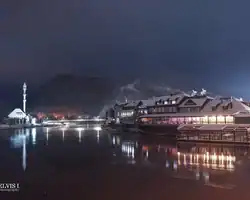 Noćni pogled na Krušnicu s osvijetljenom obalom i planinama u pozadini, odražavajući se u vodi. Prekrasan pogled na Krušnicu noću s osvijetljenim obalom i planinama u pozadini.
