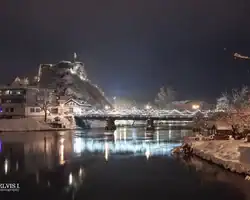 Krušnica rijeka i tvrđava na snijegu, noćni pejzaž s osvjetljenjem i odrazima na vodi. Krušnica rijeka i tvrđava na snijegu noću s refleksijama na vodi.