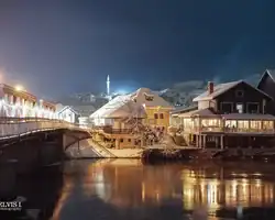 Krušnica noću s osvijetljenim kućama i mostom, odraz u rijeci, planine u pozadini. Noćni prizor Krušnice s osvjetljenim kućama i mostom.