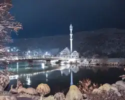 Krušnica rijeka s mostom i minaretom u zimskom okruženju noću, odraz u vodi. Krušnica rijeka i most s minaretom u zimskom okruženju noću.