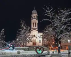 Crkva u snijegu s osvjetljenjem, zimskim drvećem i ulicom u pozadini, noćna scena u Bosni i Hercegovini. Crkva u snijegu s osvjetljenjem u noći, okružena zimskim drvećem.