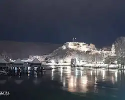 Krušnica noću s osvijetljenim dvorcem i odrazom u rijeci, snježni pejzaž, mirna atmosfera. Prekrasan snježni pejzaž Krušnice s osvijetljenim dvorcem na brdu.