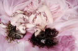 Daughter twirling in pink princess dress while mother watches lovingly. Studio portrait of mother with daughter in pink princess dresses – children’s photography NYC