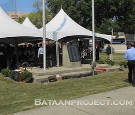 The American and Filipino flags fly on both sides of the memorial marker with the names of the National Guard members of B Company. Flags and plaque