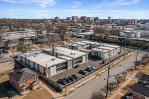 Aerial view of contemporary residential apartments with parking, surrounded by trees and city skyline.
