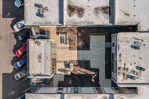 Aerial view of a city apartment rooftop featuring parking spaces, outdoor seating, and a small landscaped area.