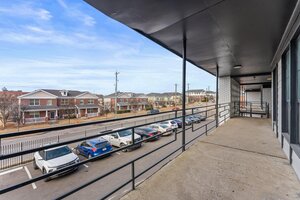 Bright, spacious balcony with black railings in an apartment complex, with street view of houses and parked cars.