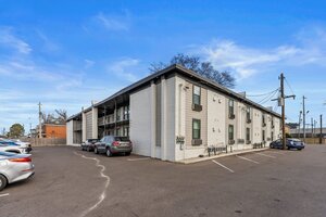 Contemporary apartment building with parking, located in a vibrant urban area under clear blue skies.