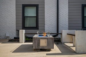 Contemporary outdoor fire pit with blue flames, surrounded by concrete benches on modern patio, house in background.