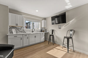 Bright kitchen featuring sleek white cabinetry, marble accents, and contemporary black bar stools.