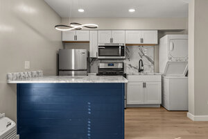 Spacious kitchen featuring stainless appliances, white cabinets, and marble backsplash.