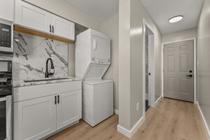 Laundry room with stacked washer and dryer, sleek marble backsplash, and bright white cabinets.