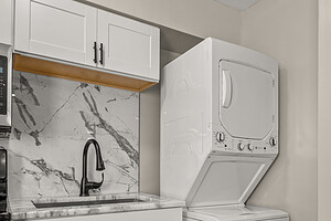 Modern laundry space with stacked washer and dryer, white cabinets, black faucet, and marble backsplash.