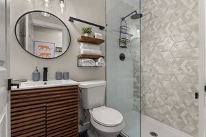 Stylish bathroom featuring wood vanity, glass shower enclosure, and contemporary accessories.