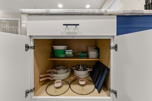 Kitchen cabinet organized with pots, pans, lids, and storage containers for efficient cooking space.