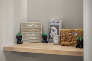 Decorative shelf with Memphis-themed sign, small potted succulents, art print, candle, and woven basket.