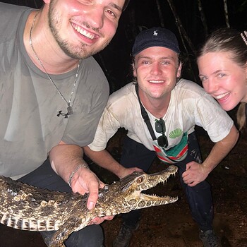 Three people holding small crocodile jungle night 2026 05