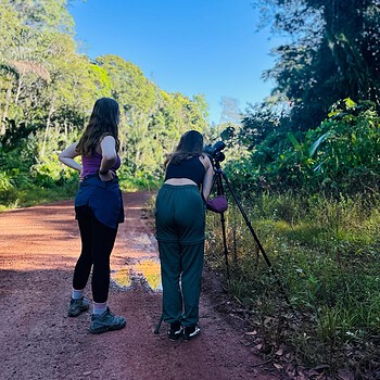 Two women camera tripod forest road 2026 05
