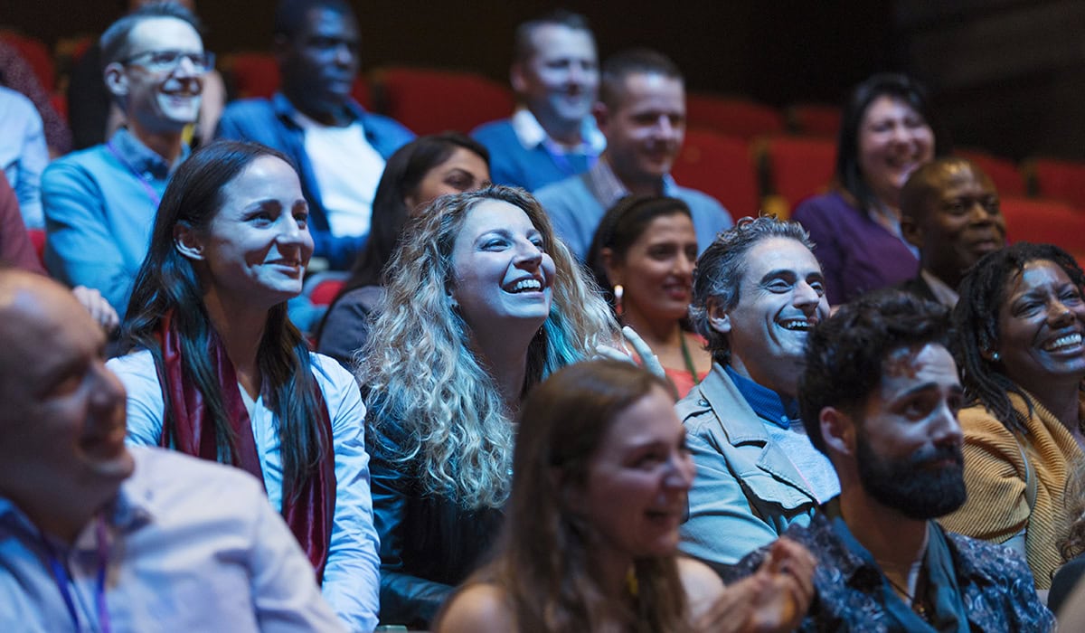 Smiling, Enthusiastic Audience In Dark Auditorium