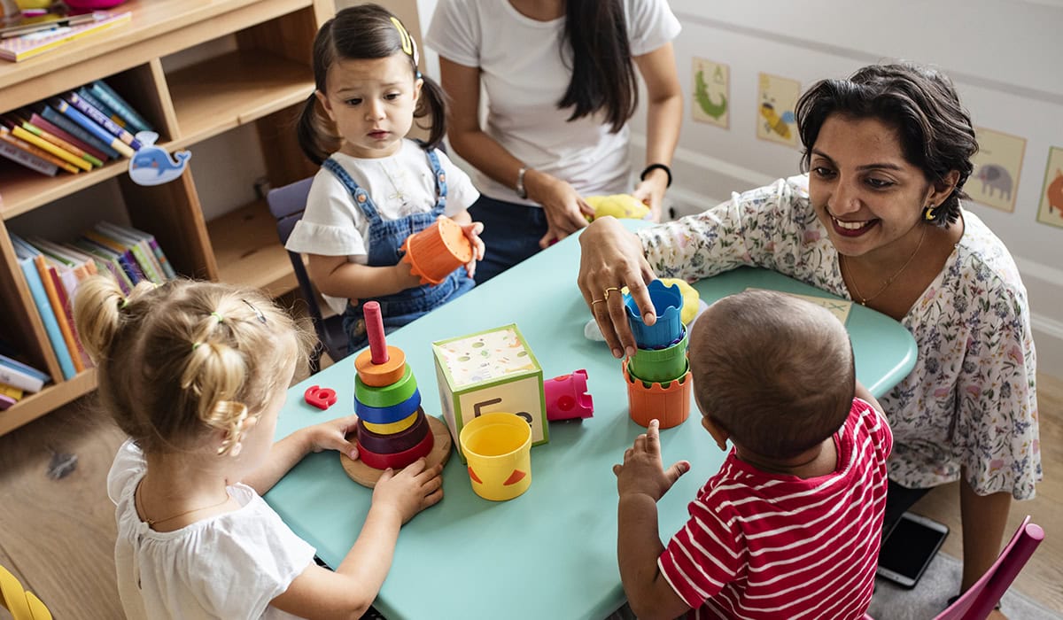 Nursery Children Playing With Teacher In The Classroom