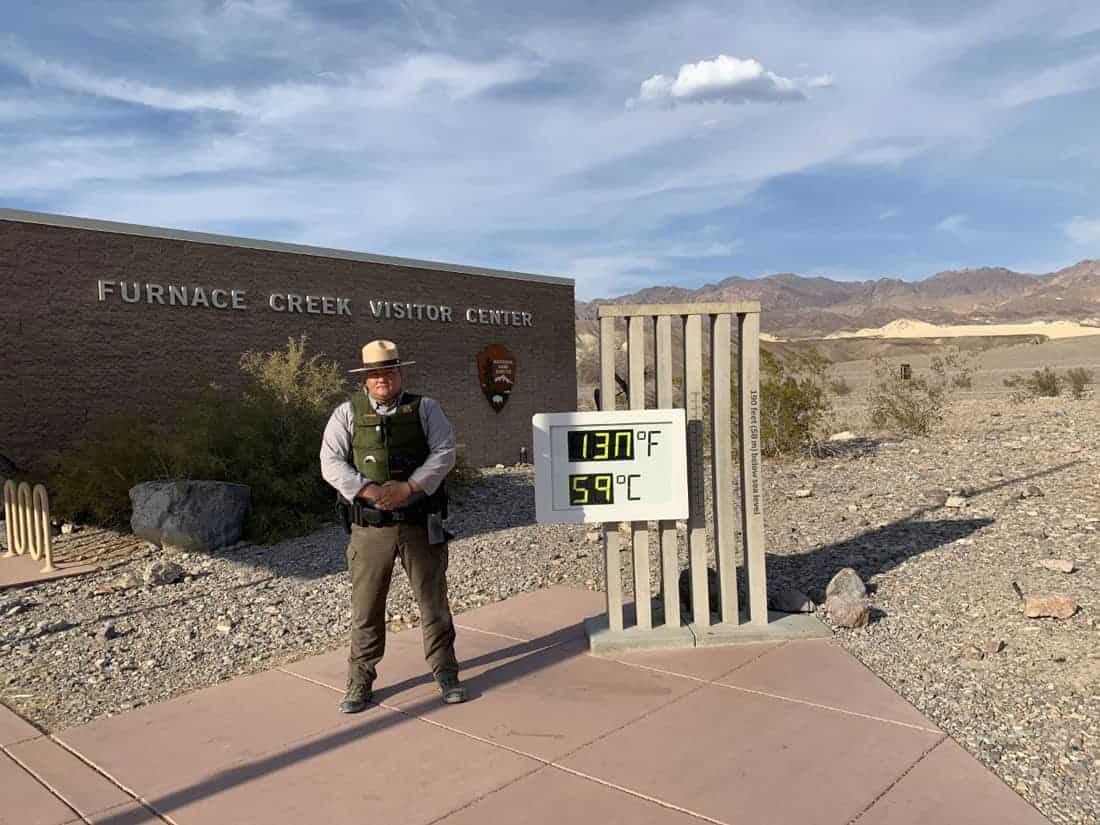 A ranger stands next to the thermometer at Furnace Creek Visitor Center. The Celsius reading should display 54 degrees. Photo: NPS, public domain.