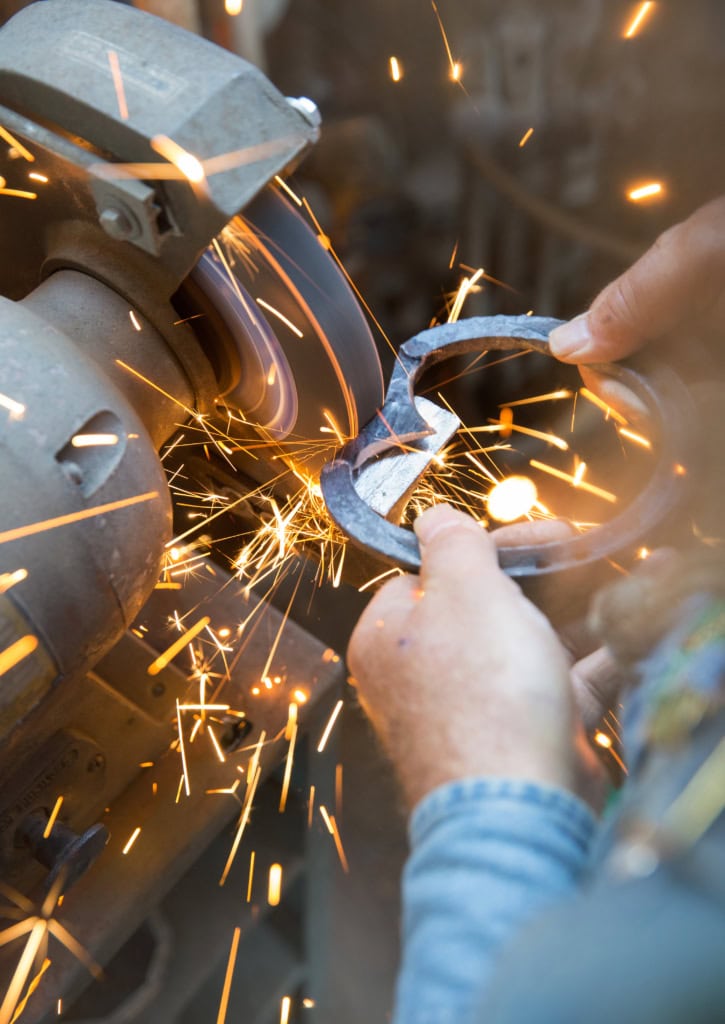 Hufschmied mit Hufeisen an Schleifmaschine, sprühende Funken
