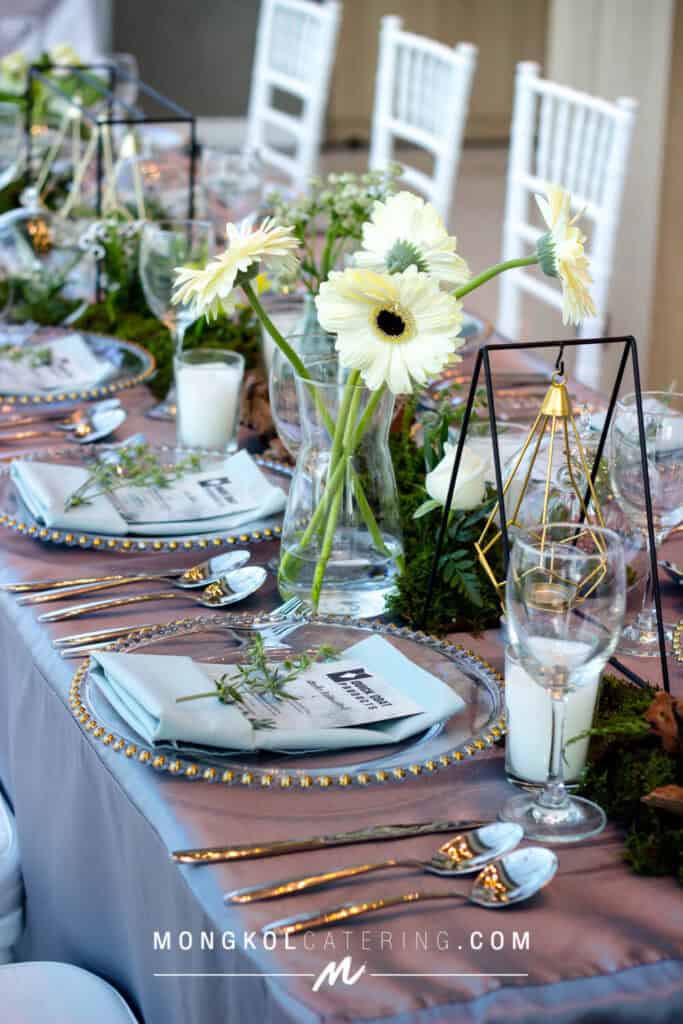 Soft white gerbera daisies centerpiece at Thailand wedding catering event, elegant table setup with gold accents.