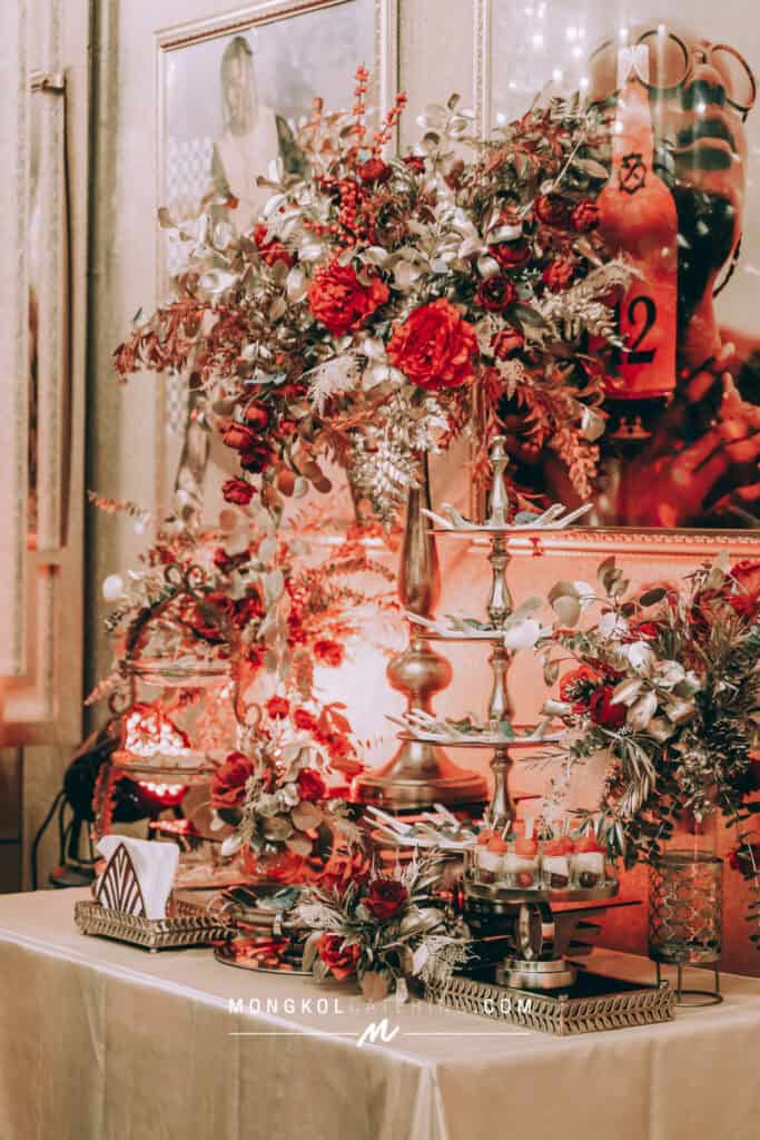 Elegant floral centerpiece with red roses and greenery at Mongkol Catering event in Thailand.
