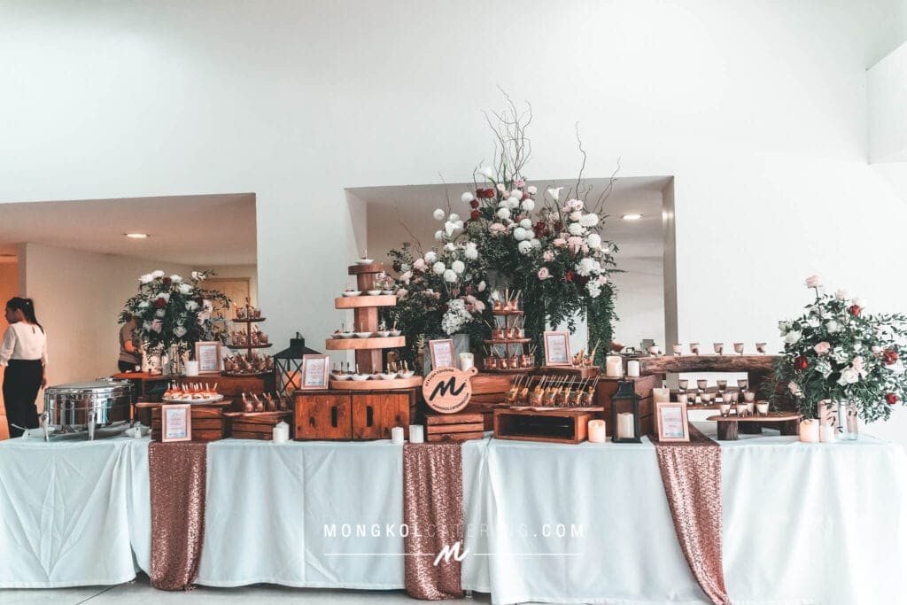 Elegant wedding dessert table with floral arrangements, chocolate treats, and candles in Thailand.