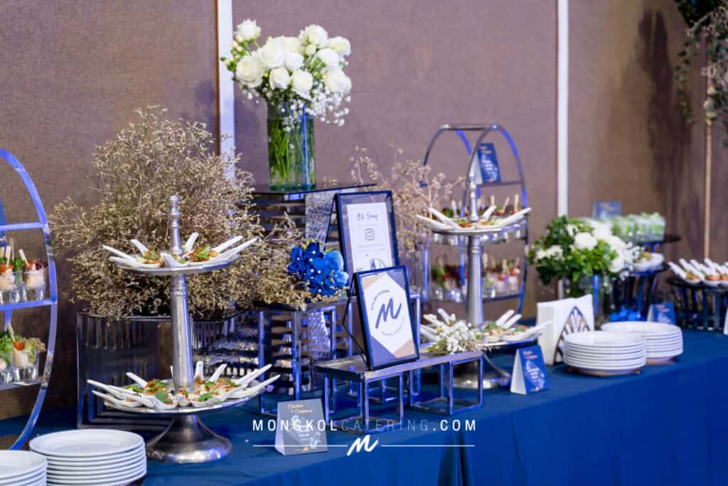 Elegant event catering setup with floral decorations in Thailand, featuring plated appetizers and tableware.